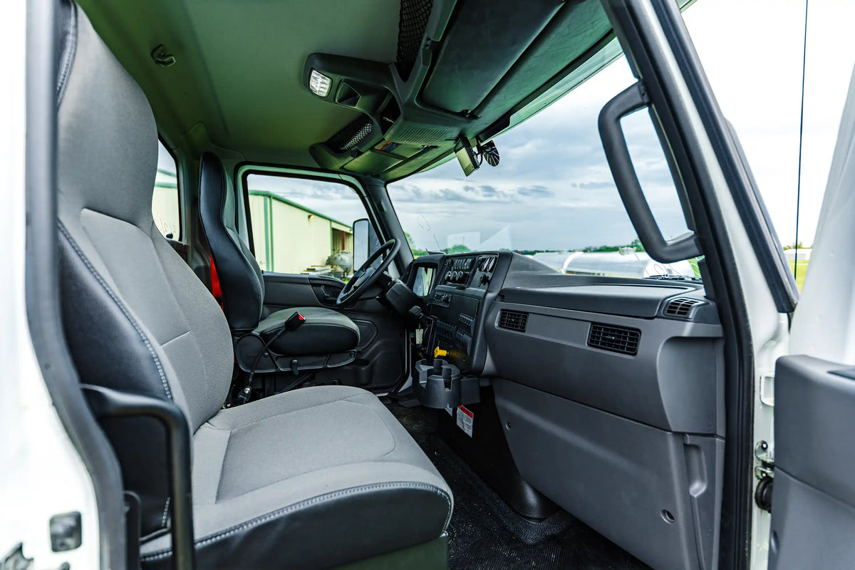 The passenger-side interior truck cab of the 2026 International MV-607 1900 Gallon Vacuum Truck for sale from Arkson Truck Co, showing the passenger's seat, dashboard, and storage with a clouded sky visible through the windshield.