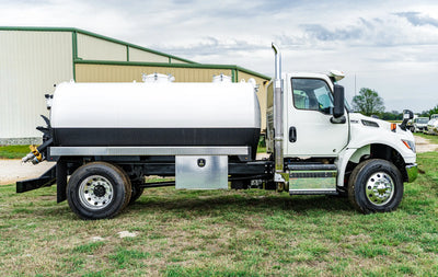 Passenger-side profile image of the 2026 International MV-607 1900 Gallon Vacuum Truck for sale from Arkson Truck Co parked in front of an industrial building with other vocational  trucks in the background