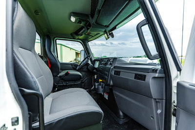 The passenger-side interior truck cab of the 2026 International MV-607 1900 Gallon Vacuum Truck for sale from Arkson Truck Co, showing the passenger's seat, dashboard, and storage with a clouded sky visible through the windshield.