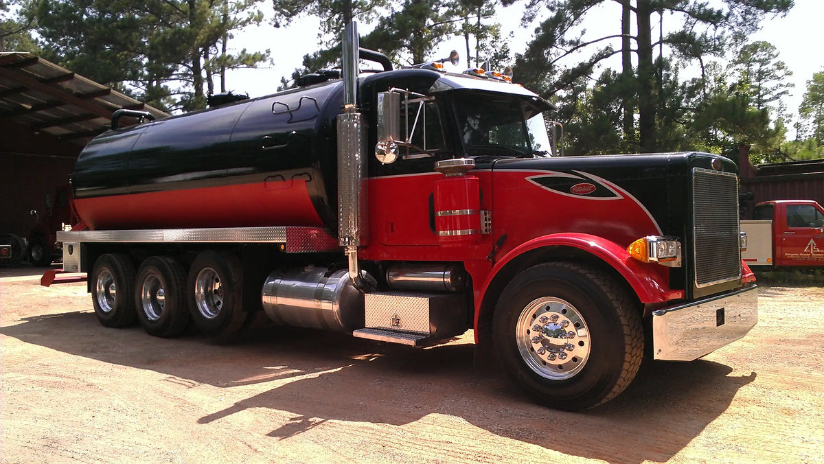 A red and black industrial vacuum truck built by Arkson Truck Co for septic and sewer pumping applications, parked outdoors on a dirt lot with trees and a shed visible in the background.