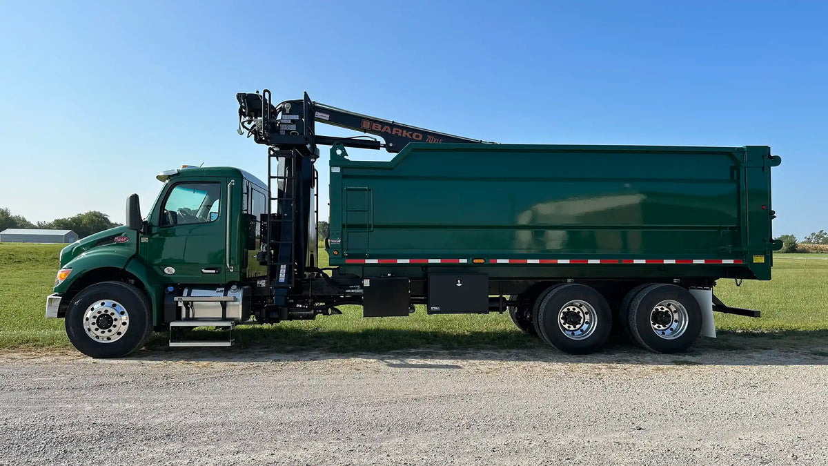 Green custom grapple truck built by Arkson Truck Co with a heavy-duty dump body for tree service and construction debris clean up, parked outdoors on a gravel lot with grass and a barn in the background.